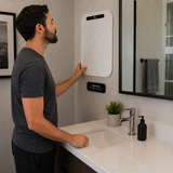 Man interacting with a white electronic device mounted on a bathroom wall.